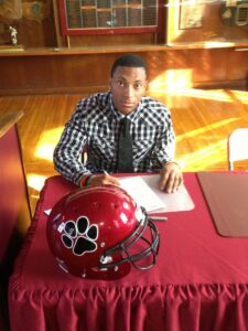 young man signing papers with a football helmet